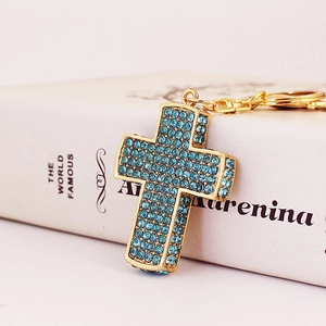 Goldener Kreuz-Schlüsselanhänger mit himmelblauen Strasssteinen auf einem Buchhintergrund