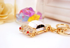 Close-up of golden car keychain with white enamel finish and shimmering crystal inlay