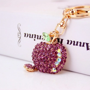 Sparkling purple apple keychain with rhinestones and gold base on a classic book backdrop