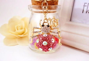 Detailed macro of pink rhinestone spider keychain hanging on a glass bottle neck