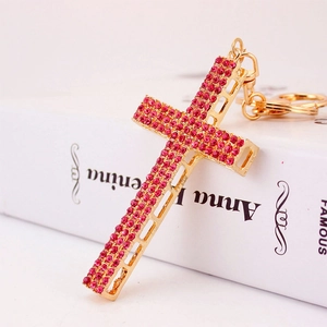 Elegant gold metal cross keychain with rose pink rhinestones on a white book surface