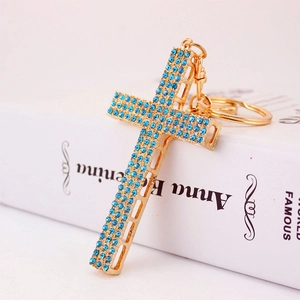 Elegant gold cross keychain with blue rhinestones on a white book for accessories