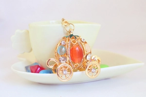 Detail of a golden pumpkin carriage keychain with rhinestones hanging on a coffee cup