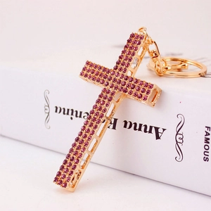 Religious gold cross keychain featuring sparkling purple crystals on a white book surface