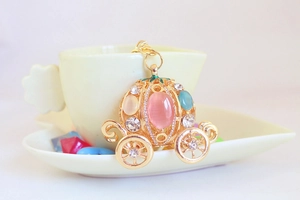Detailed view of a gold pumpkin carriage keychain with pink gemstone on a ceramic cup