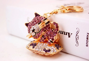 Dettaglio di un portachiavi a forma di gatto con strass viola su cuscino dorato e catena