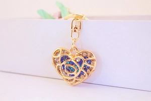 Macro shot of heart-shaped gold keychain with blue rhinestones and hollow rose patterns