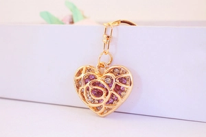Close-up of golden hollow heart keychain with pink rhinestones and floral pattern