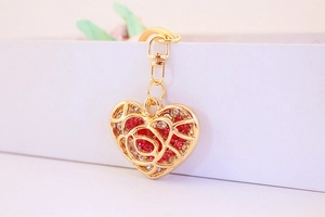 Detail of heart-shaped hollow rose keychain with red rhinestones in golden finish