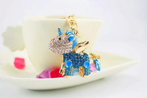 Detail of a gold plated unicorn keychain with inlaid white and blue crystals on a ceramic cup