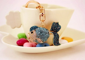 Detailed close-up of a sparkling gold goldfish keychain with blue rhinestones on a cup