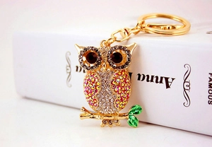 Close-up of golden owl keychain with pink rhinestones and green enamel branch detail