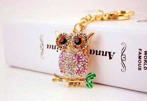 Detail of owl keychain with sparkling crystals and green enamel leaf on golden metal