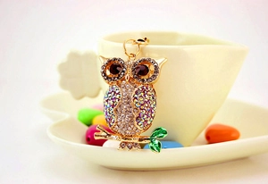 Detailed close-up of a colorful crystal owl keychain with emerald green enamel leaves