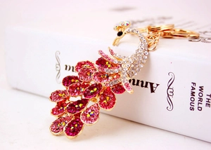 Close-up of a golden peacock keychain with pink and white rhinestones on a book