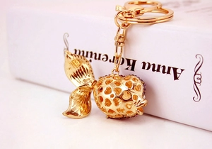 Detail of a hollow heart-shaped gold keychain with purple rhinestones and fish tail pendant