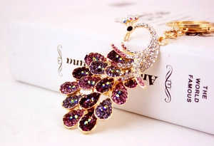 Detail view of a colorful peacock keychain with purple and white rhinestones on gold metal