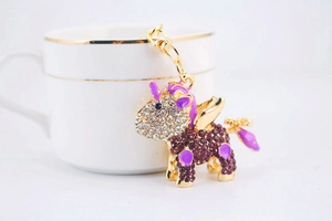 Close-up of a golden unicorn keychain with purple enamel wings and sparkling rhinestones