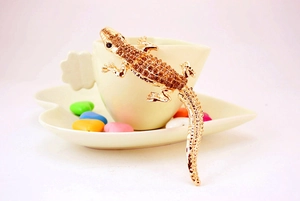 Macro detail of a gold-plated gecko keychain adorned with amber rhinestones on a white cup