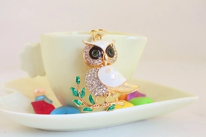 Detail of owl keychain with white enamel, green crystal eyes, and rhinestones on a cup