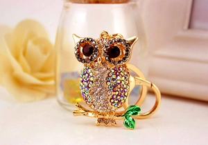 Close-up of owl keychain with colorful crystals, golden alloy finish, and green enamel leaves