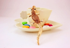 Detailed macro view of a gold lizard brooch with sparkling brown crystals on a white cup
