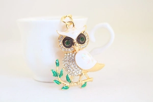 Close-up of golden owl keychain featuring white enamel wings and sparkling rhinestones