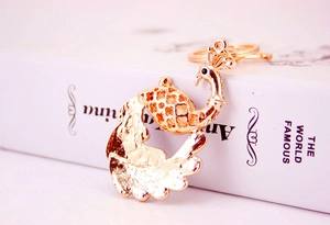 Close-up of rose gold peacock metal keychain with hollow pattern hanging on a white book