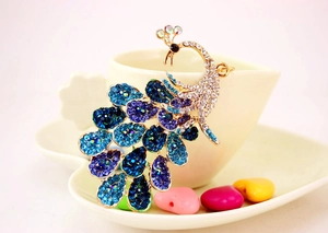 Detail of colorful crystal peacock keychain hanging on a white heart ceramic cup