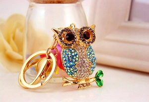 Detail of colorful owl keychain with blue crystals and gold base on a floral background