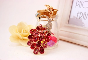 Close-up of golden peacock keychain with red and pink rhinestones on a decorative glass