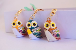 Three colorful owl keychains with rhinestones and gold chains in a diagonal layout