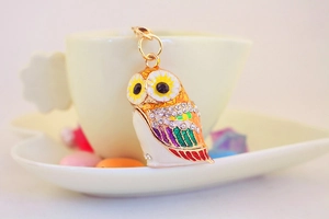 Close-up of a colorful enamel owl keychain with rhinestones hanging on a beige coffee cup