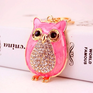 Porte-clés hibou rose avec strass blancs et métal doré sur un fond de livre blanc
