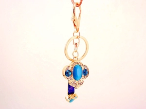 Detail of a gold-plated keychain with a blue cat-eye stone and crystal cloud motif