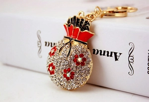 Detailed close-up of a golden money bag keychain with sparkling rhinestones and red floral accents
