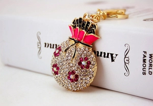 Macro detail of money bag keychain with gold plating, white crystals, and floral enamel patterns