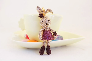 Detail of cute rhinestone rabbit keychain with purple dress next to a coffee cup