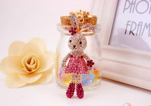 Detail of cute rhinestone bunny keychain with pink dress and golden clasp on white surface