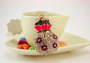 Close-up of gold coin bag keychain featuring white rhinestones and pink floral motifs
