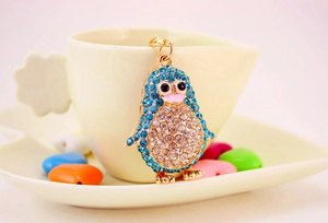 Detail of a sparkling rhinestone penguin keychain resting on a white ceramic coffee cup