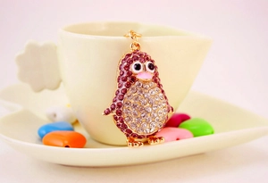 Detail of a gold penguin keychain encrusted with purple and white rhinestones