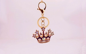 Macro detail of a sparkling gold crown keychain with purple enamel and colorful rhinestones
