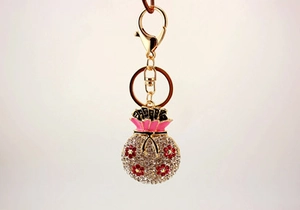 Detail of a golden fortune bag keychain with pink enamel and sparkling white rhinestones