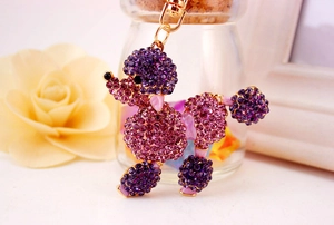 Detail shot of a purple rhinestone poodle keychain with golden metal clasp on a floral background
