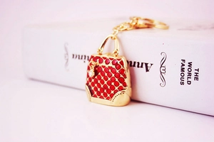 Detail of red quilted handbag keychain with gold trim hanging on a white book edge