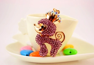 Detail eines lila Strass-Pudel-Schlüsselanhängers mit Kristallkrone auf einer Kaffeetasse