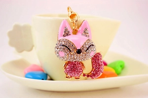 Detail of cute fox keychain with pink rhinestones on a coffee cup, gold metal finish