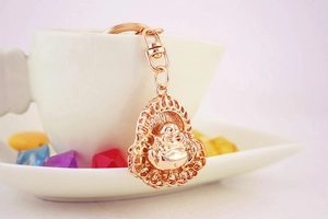 Close-up of golden Maitreya Buddha keychain hanging on a white ceramic cup edge