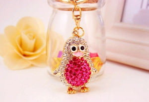 Detailed view of penguin keychain with pink rhinestones and gold base on floral background